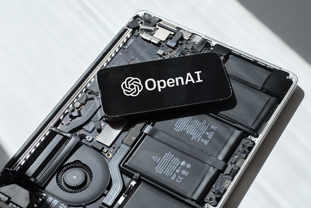 A phone showing the OpenAI logo resting on an opened laptop