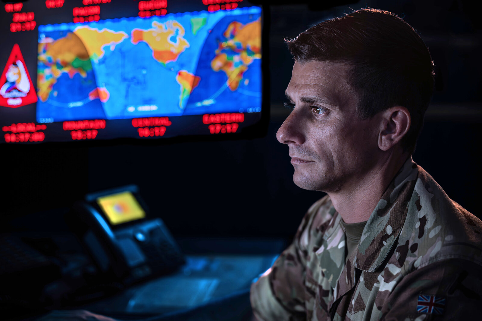 A service member watches a world map on the screens of an operations center