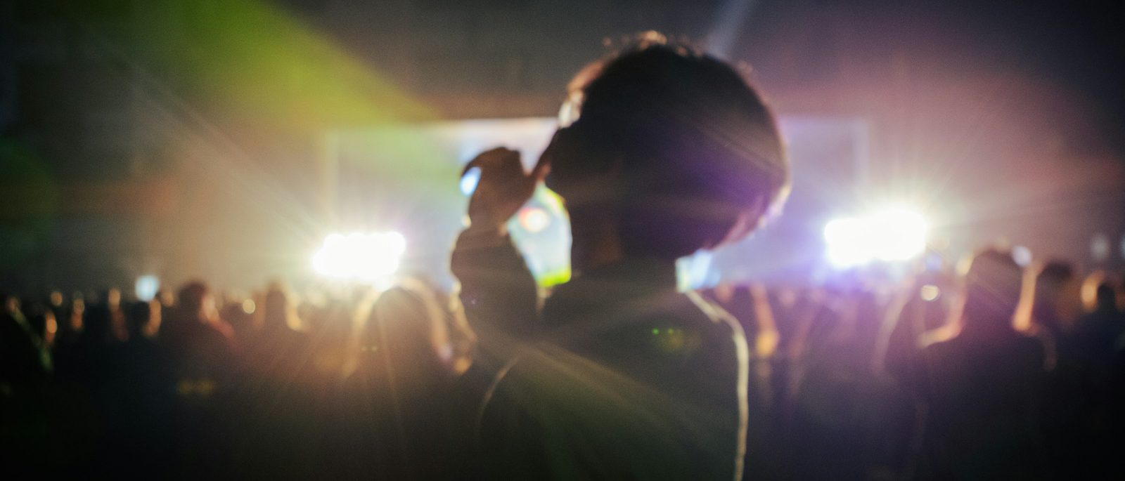 A concertgoer watches the stage while recording the performance on a phone