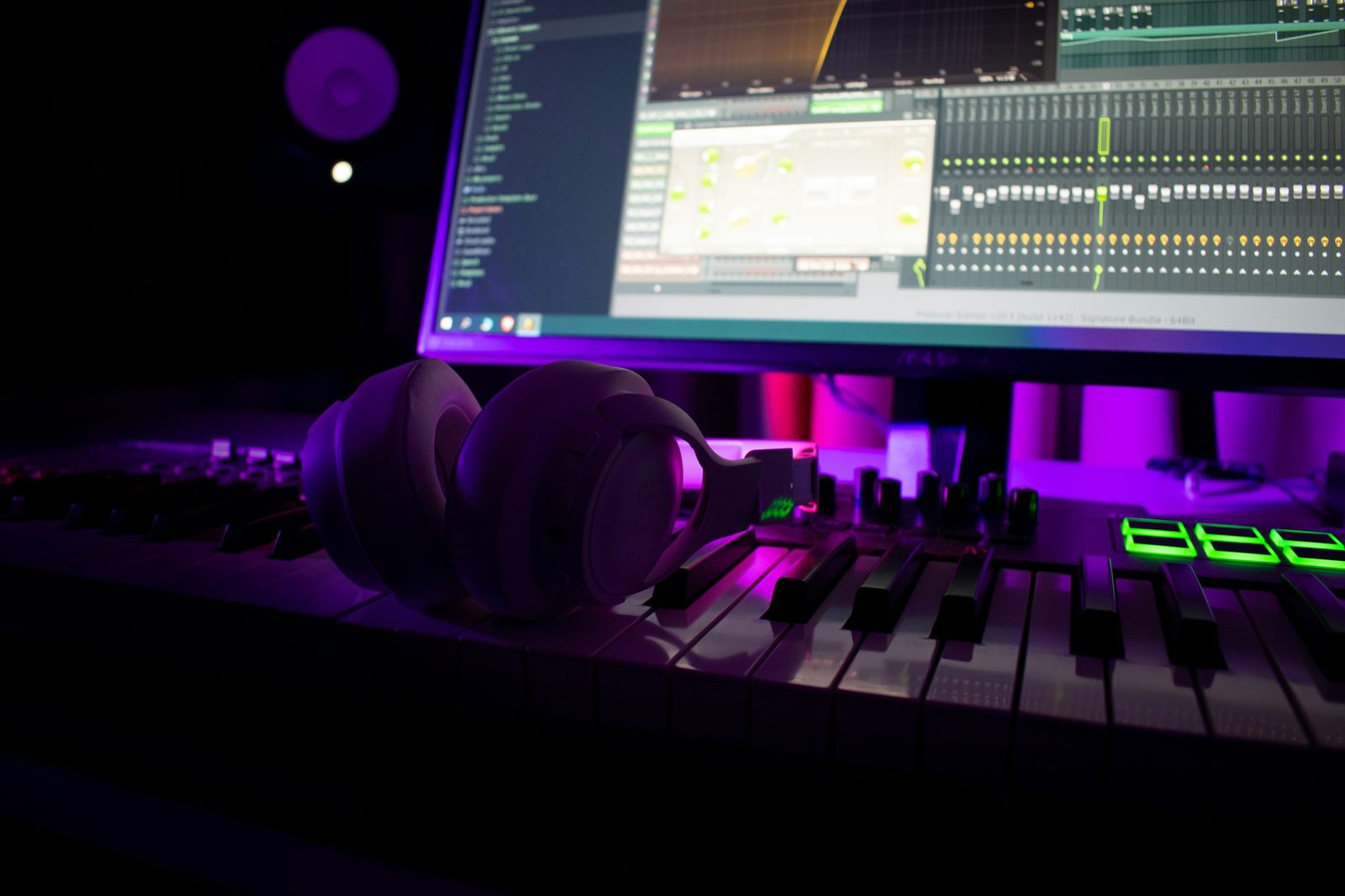 Headphones resting on a keyboard in front of a music-production workstation lit in purple and green