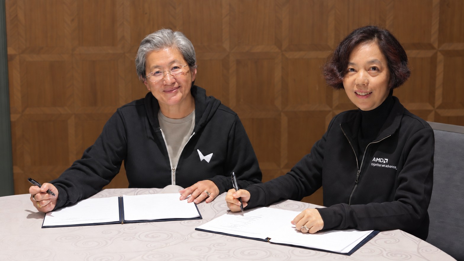 Lisa Su and Fei-Fei Li seated with documents for the AMD and World Labs agreement