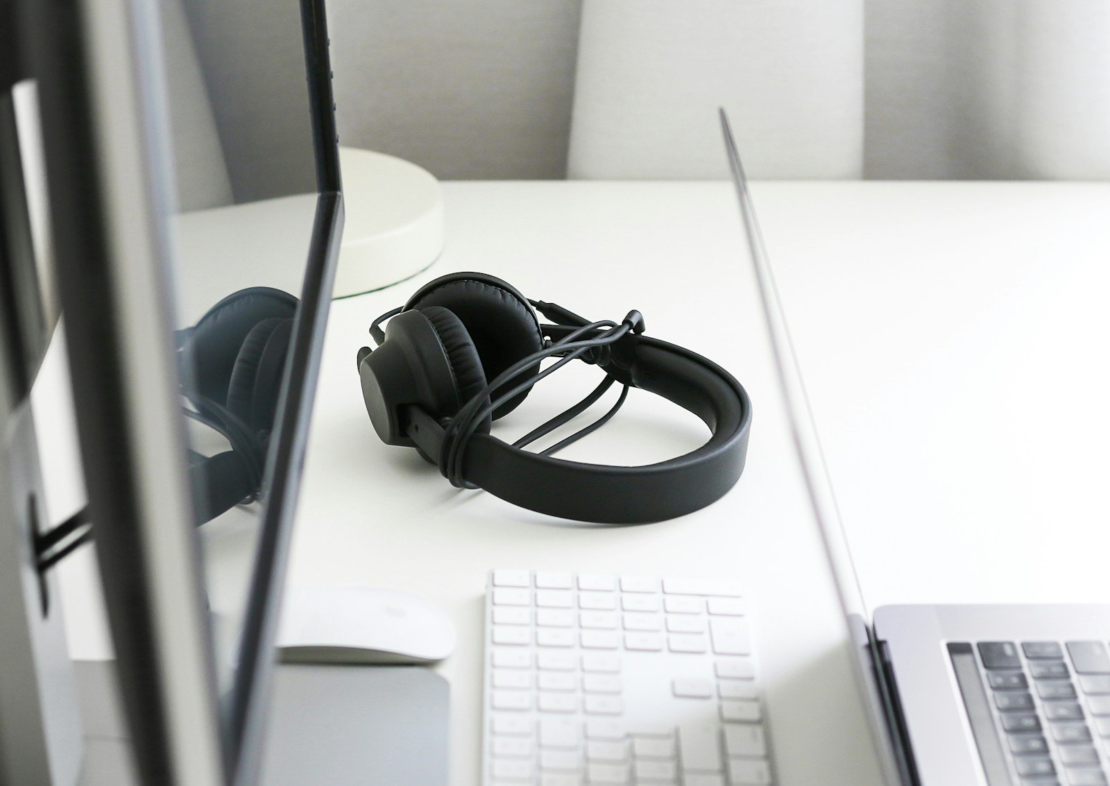 Wired headphones on a white desk next to a laptop