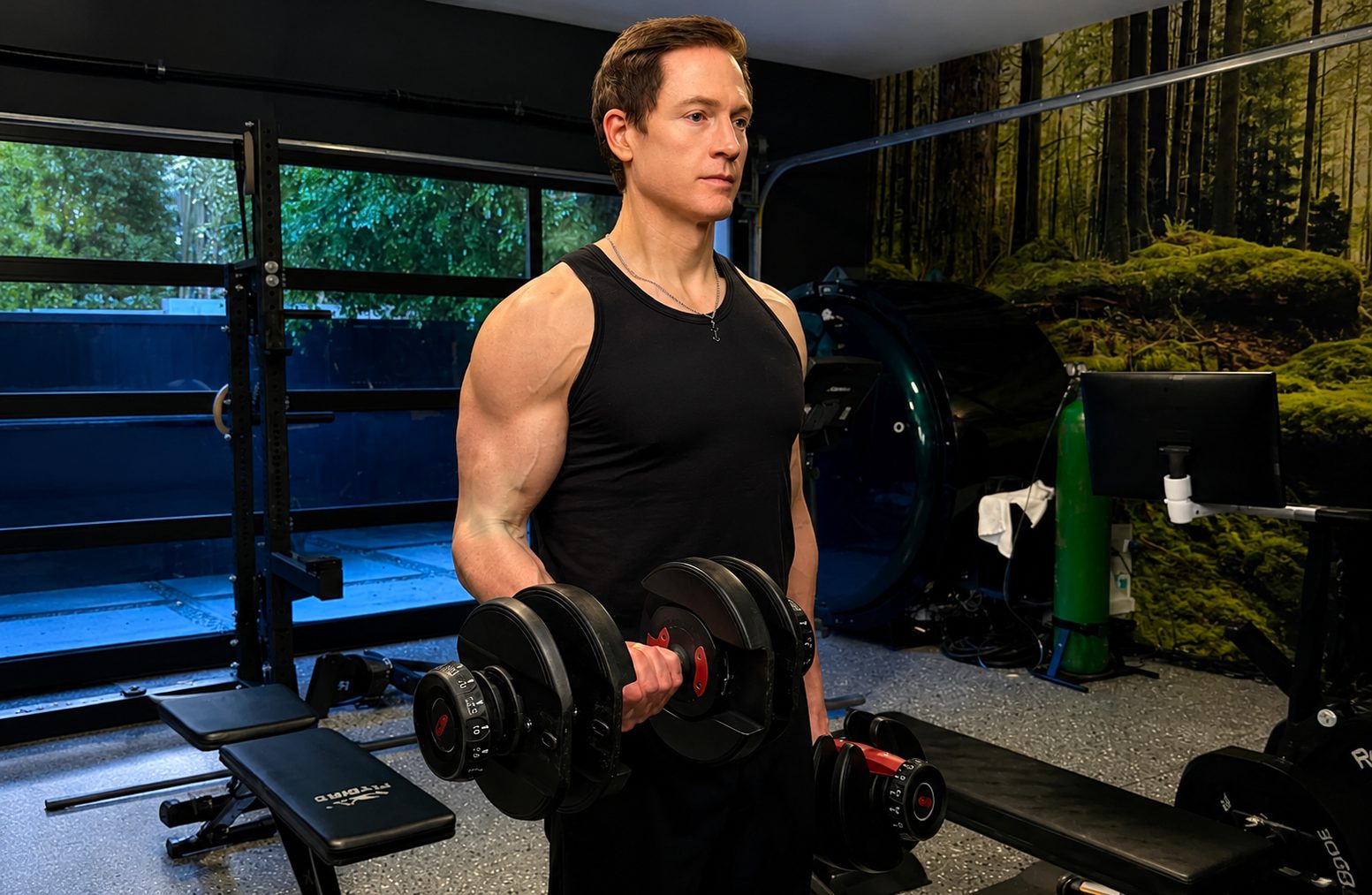 Bryan Johnson lifts dumbbells in his home gym, surrounded by measuring equipment