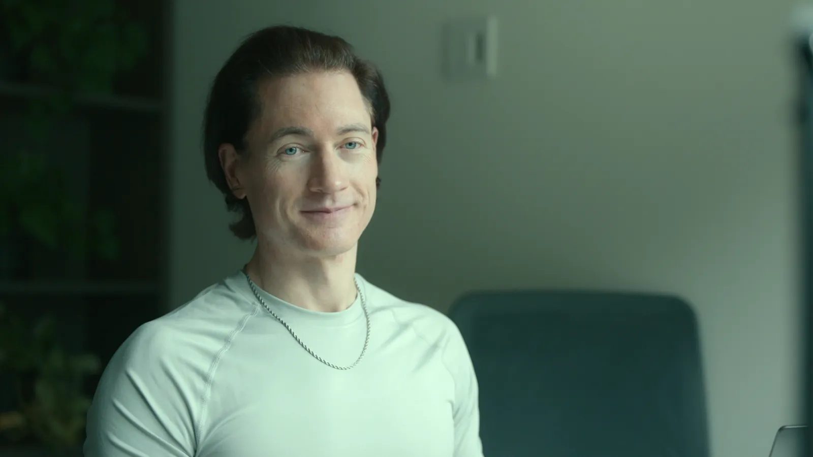 Portrait of Bryan Johnson smiling faintly, in a light T-shirt, at his home