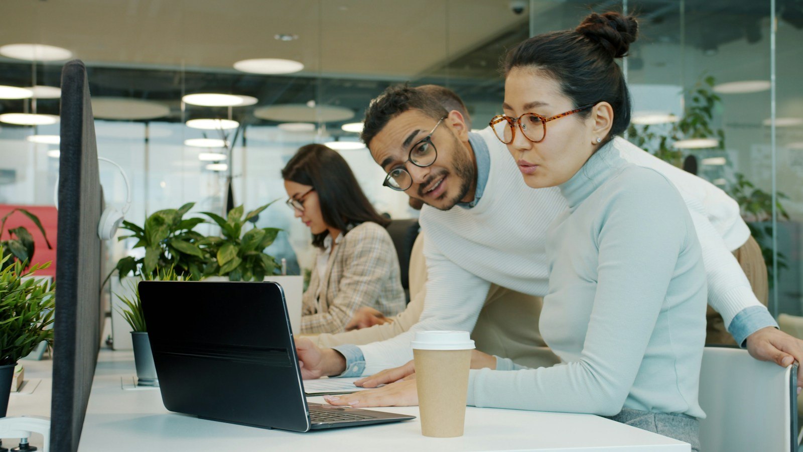 Two coworkers look at a laptop together in an office