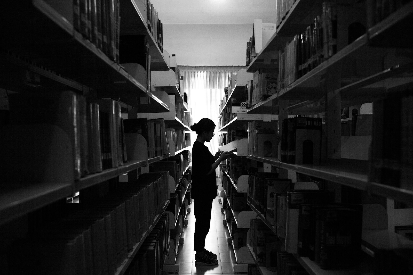 Persona consultando libros entre estanterías de una biblioteca, fotografía de contexto