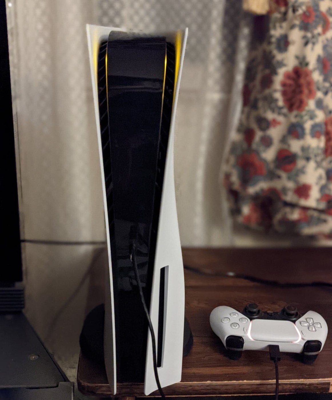 PlayStation 5 colocada en vertical sobre su soporte junto a un mando DualSense cargando