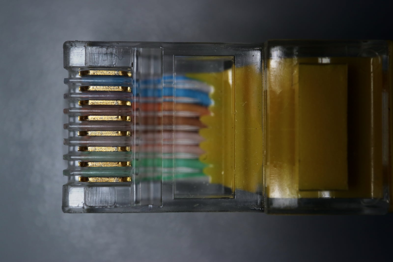 Eight metal contacts inside the transparent plug on a yellow Cat 5e Ethernet cable