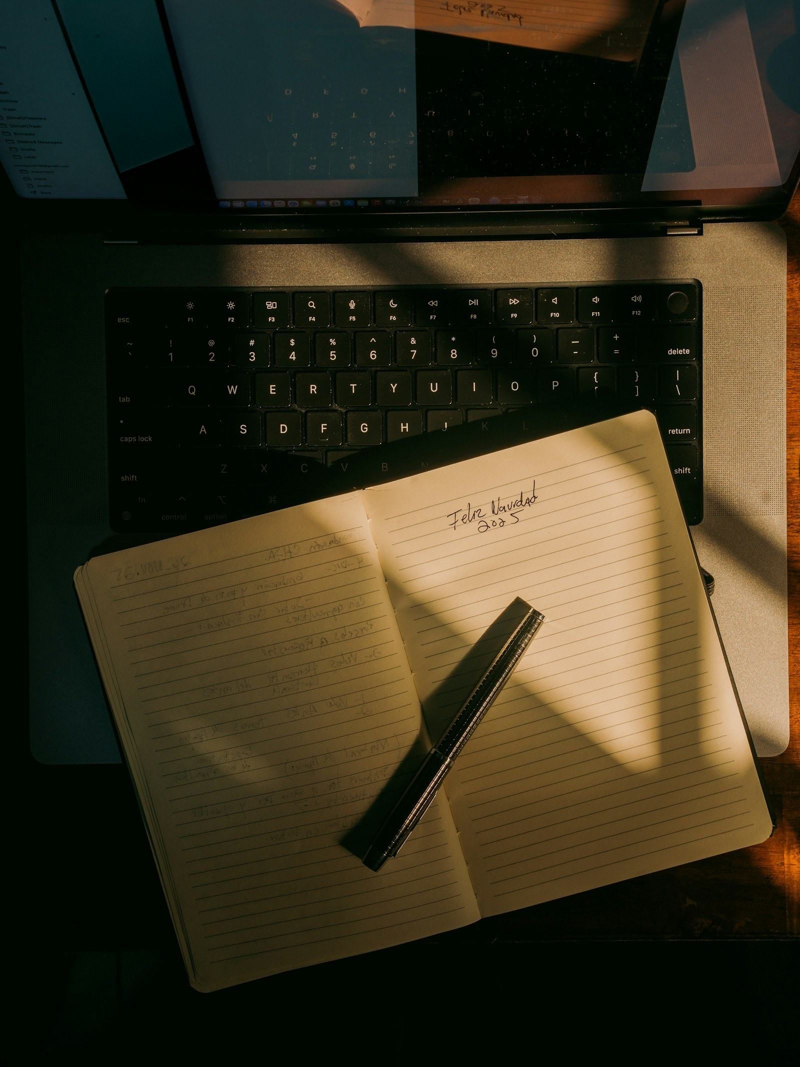 Cuaderno abierto y bolígrafo sobre el teclado de un portátil
