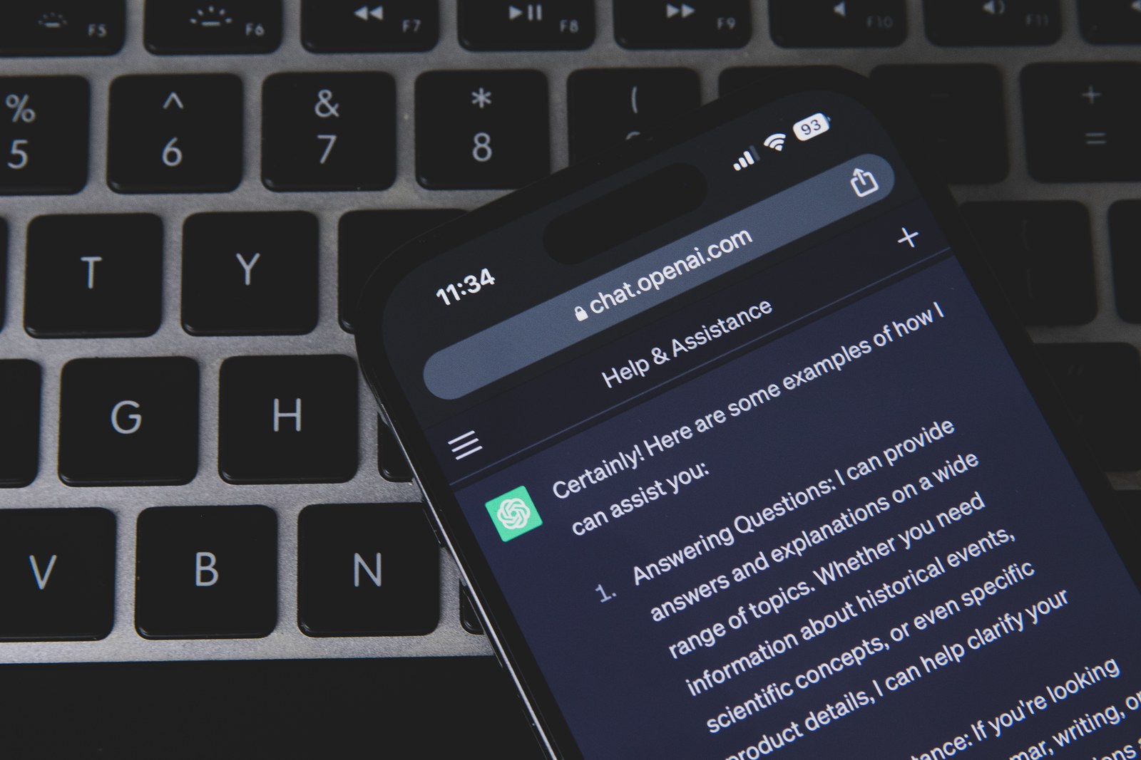 Un teléfono con la aplicación de ChatGPT abierta, apoyado sobre el teclado de un ordenador