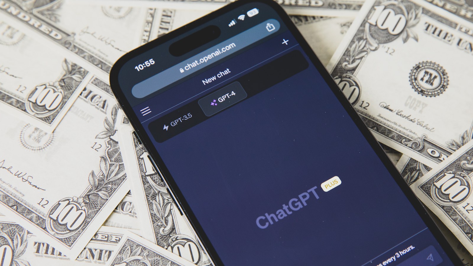 Un teléfono móvil con ChatGPT abierto, apoyado sobre billetes de dólar estadounidense