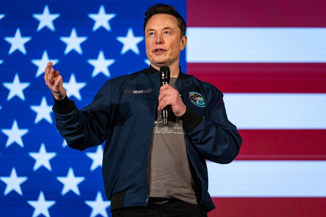 Elon Musk hablando con un micrófono delante de una bandera de Estados Unidos