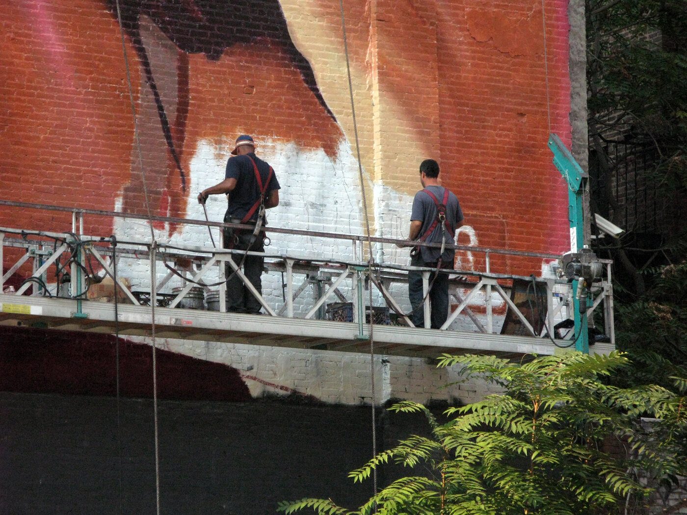 Two workers hand-paint a Grand Theft Auto advertising mural on a New York brick wall
