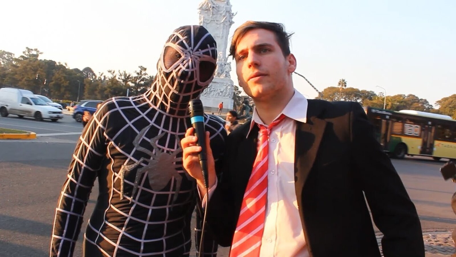 Gaspi, in a suit and tie, interviewing a man dressed as Spider-Man on a Buenos Aires street with his black tape-wrapped microphone