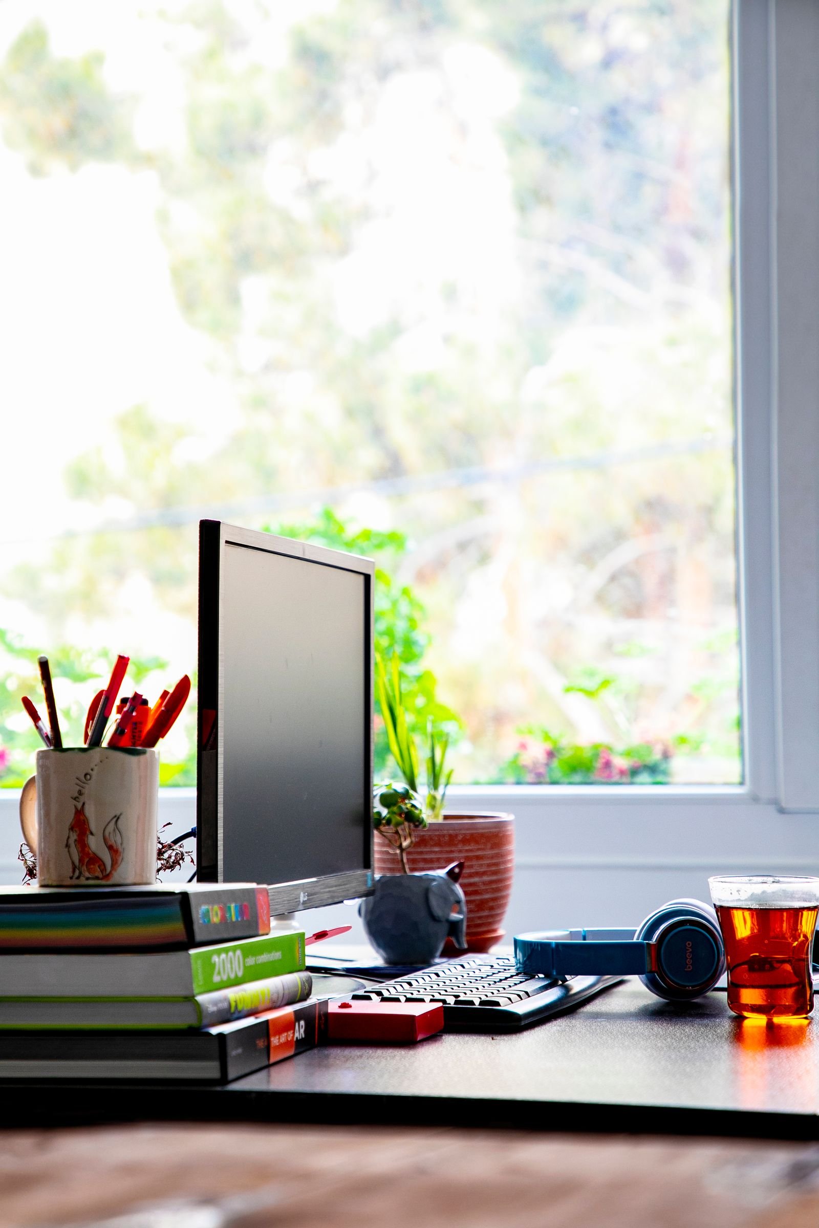 A desk with a computer, headphones and papers beside a window