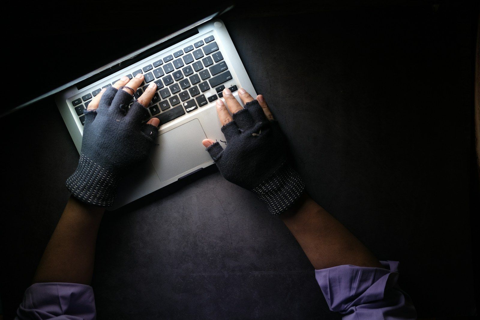 Gloved hands typing on a laptop, illustrative photograph