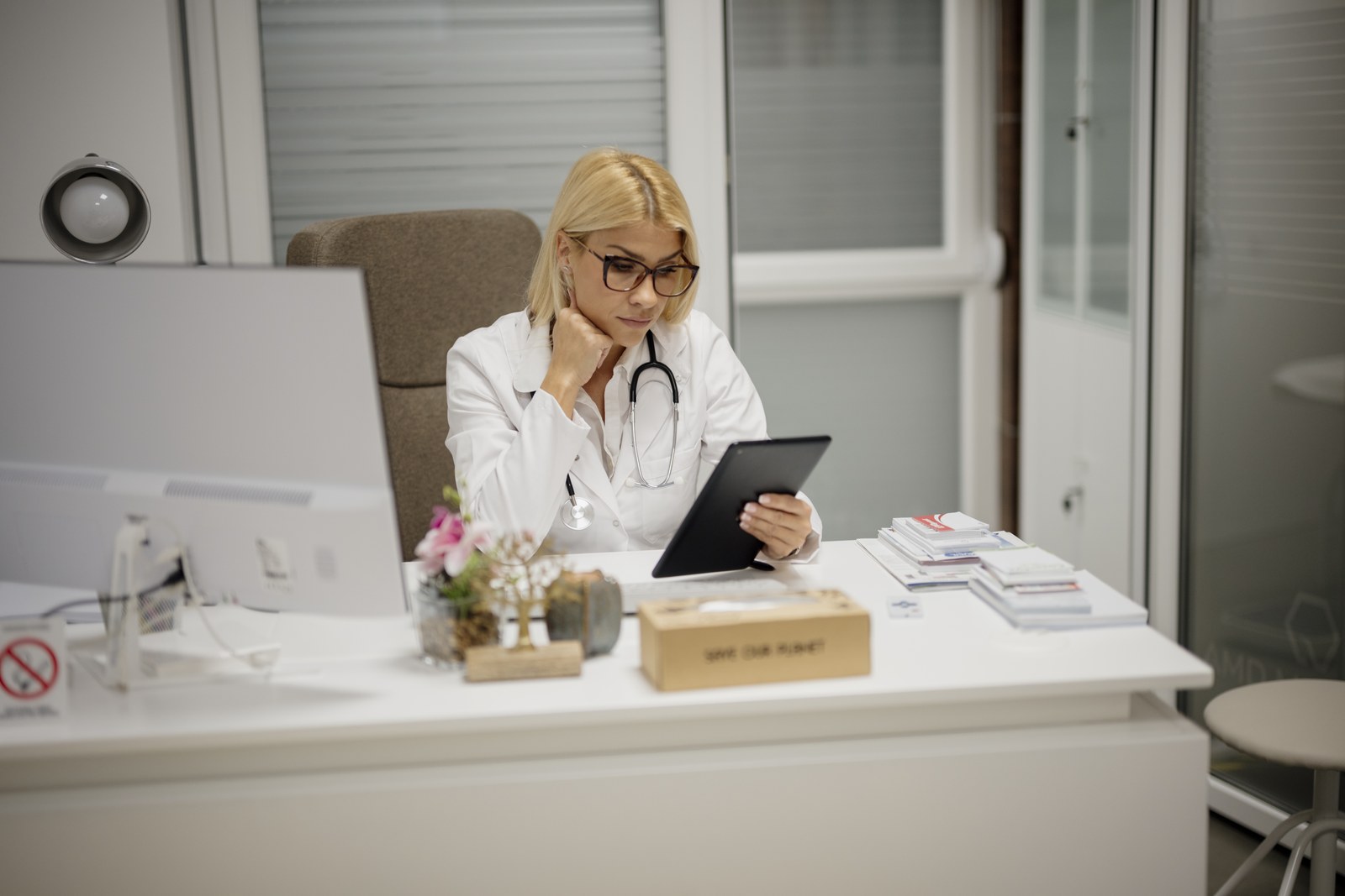 Una médica sentada en su despacho repasa en una tableta los datos de un paciente