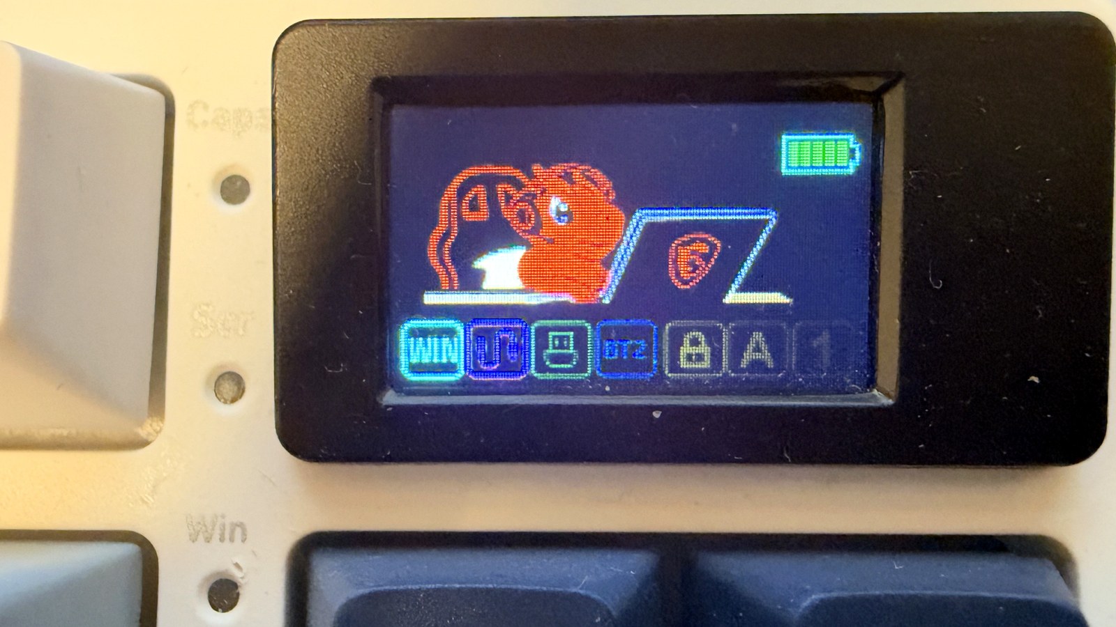 Close-up of the MSI Forge GK600's 1.06-inch screen showing MSI's mascot, a small orange dragon in front of a laptop, plus the battery gauge and mode icons, next to the navy Ins and Home keys