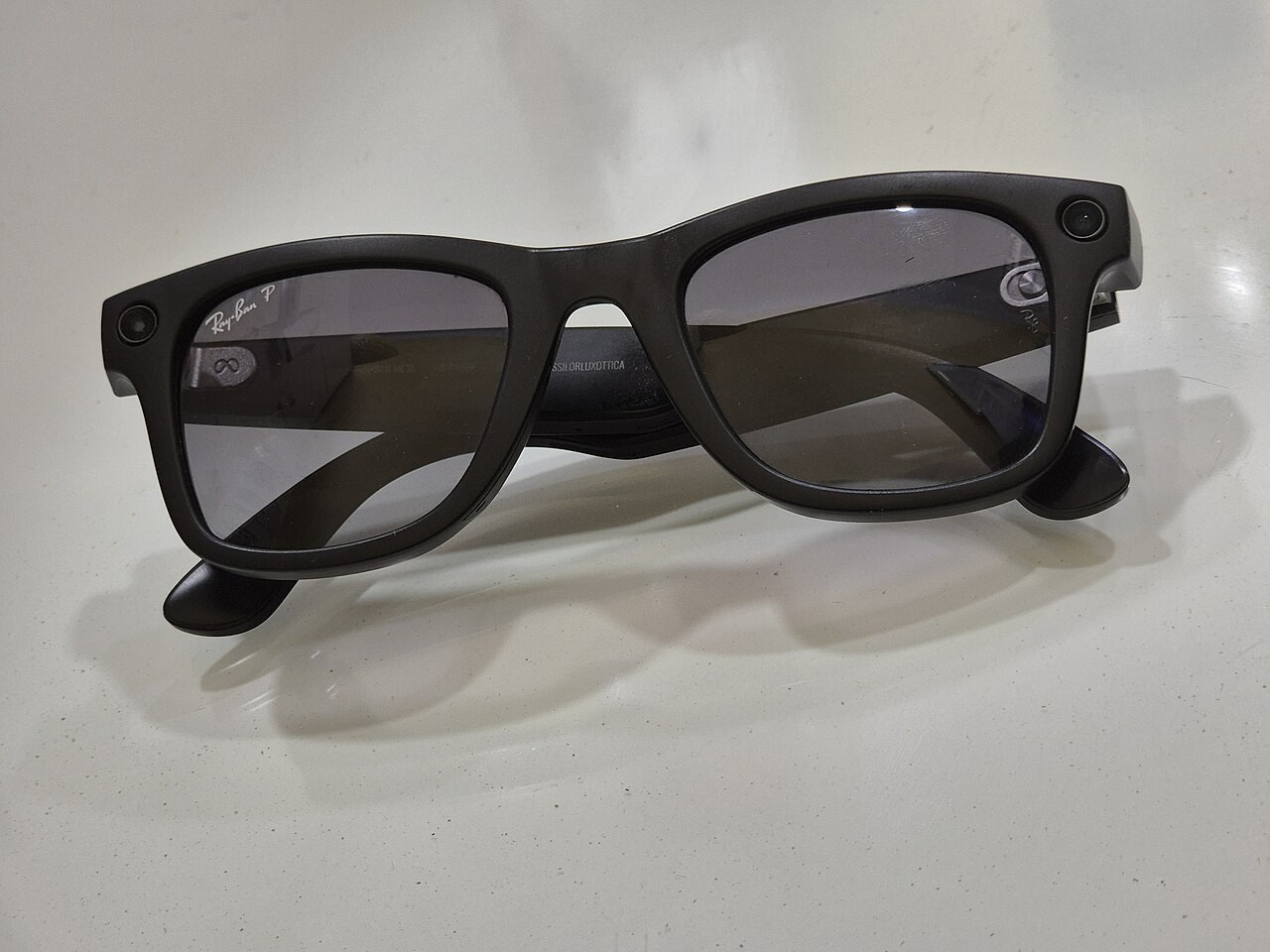 Second-generation Ray-Ban Meta Wayfarer glasses on a table, with the camera and capture light in the corners of the frame