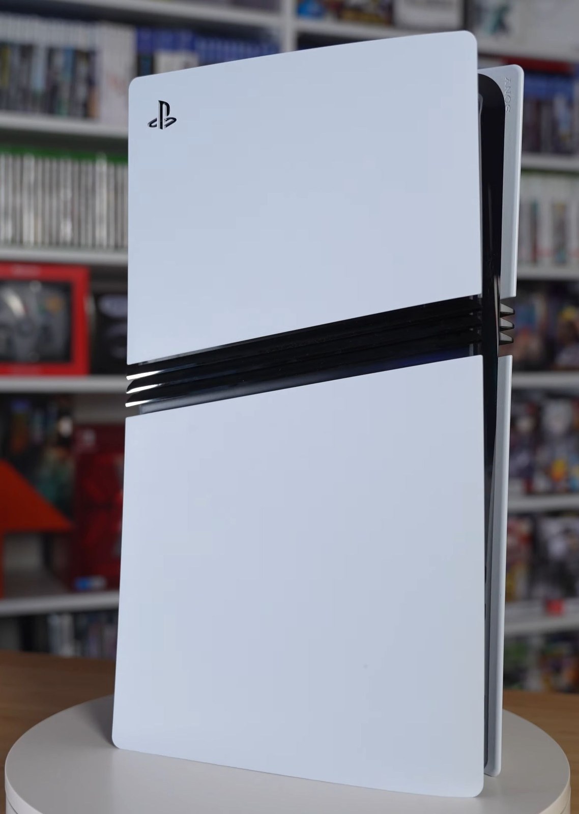 A PlayStation 5 Pro standing upright in front of a shelf of games