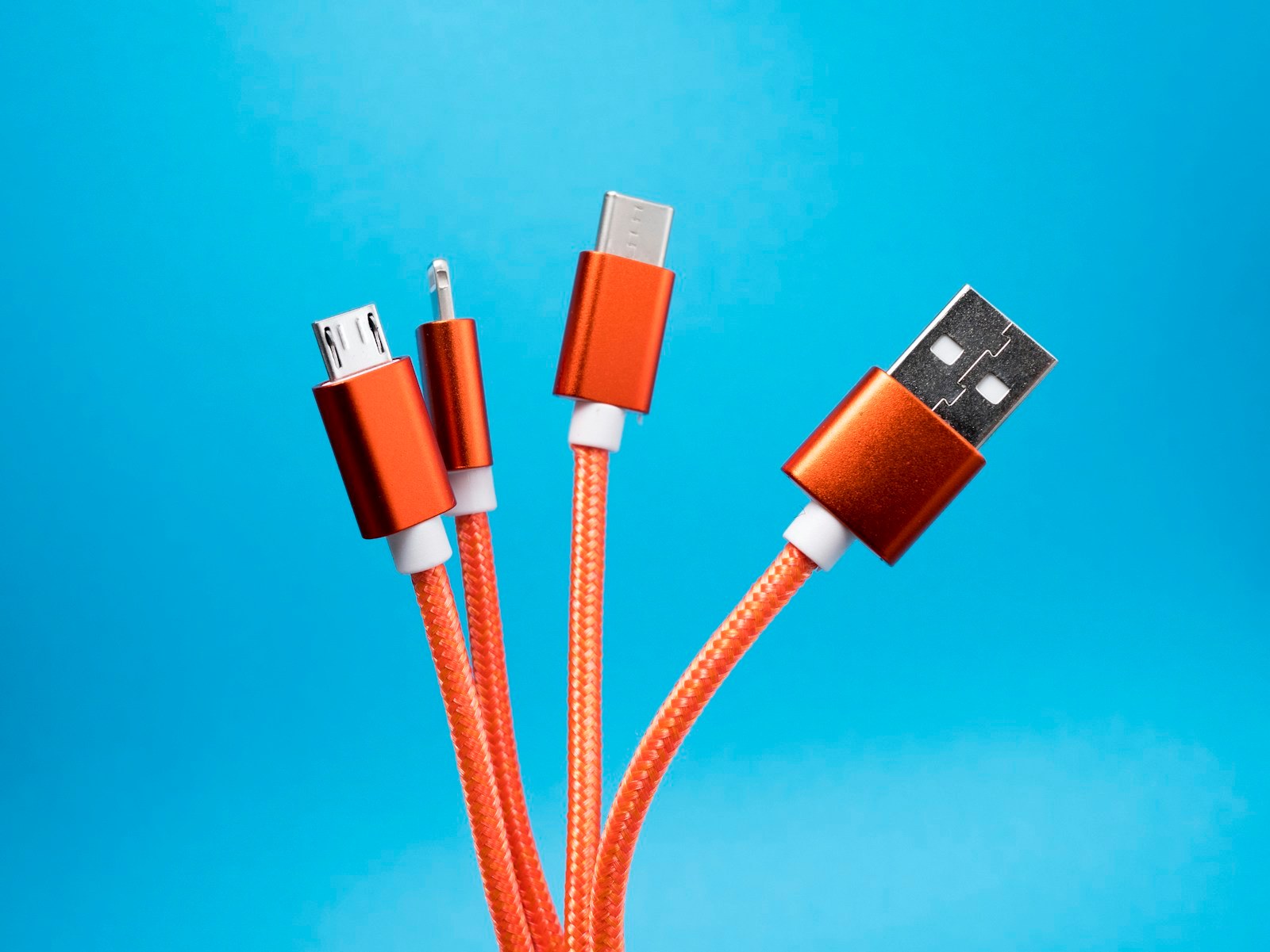 Cables naranjas con conectores USB-C, USB-A, micro-USB y Lightning sobre fondo azul