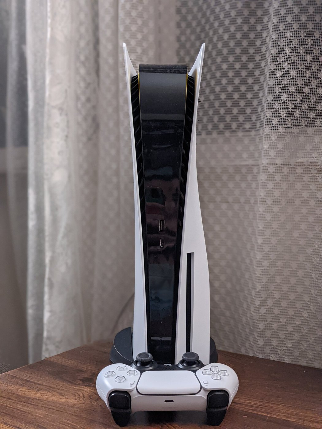 PS5 colocada en vertical sobre su soporte junto a un mando DualSense
